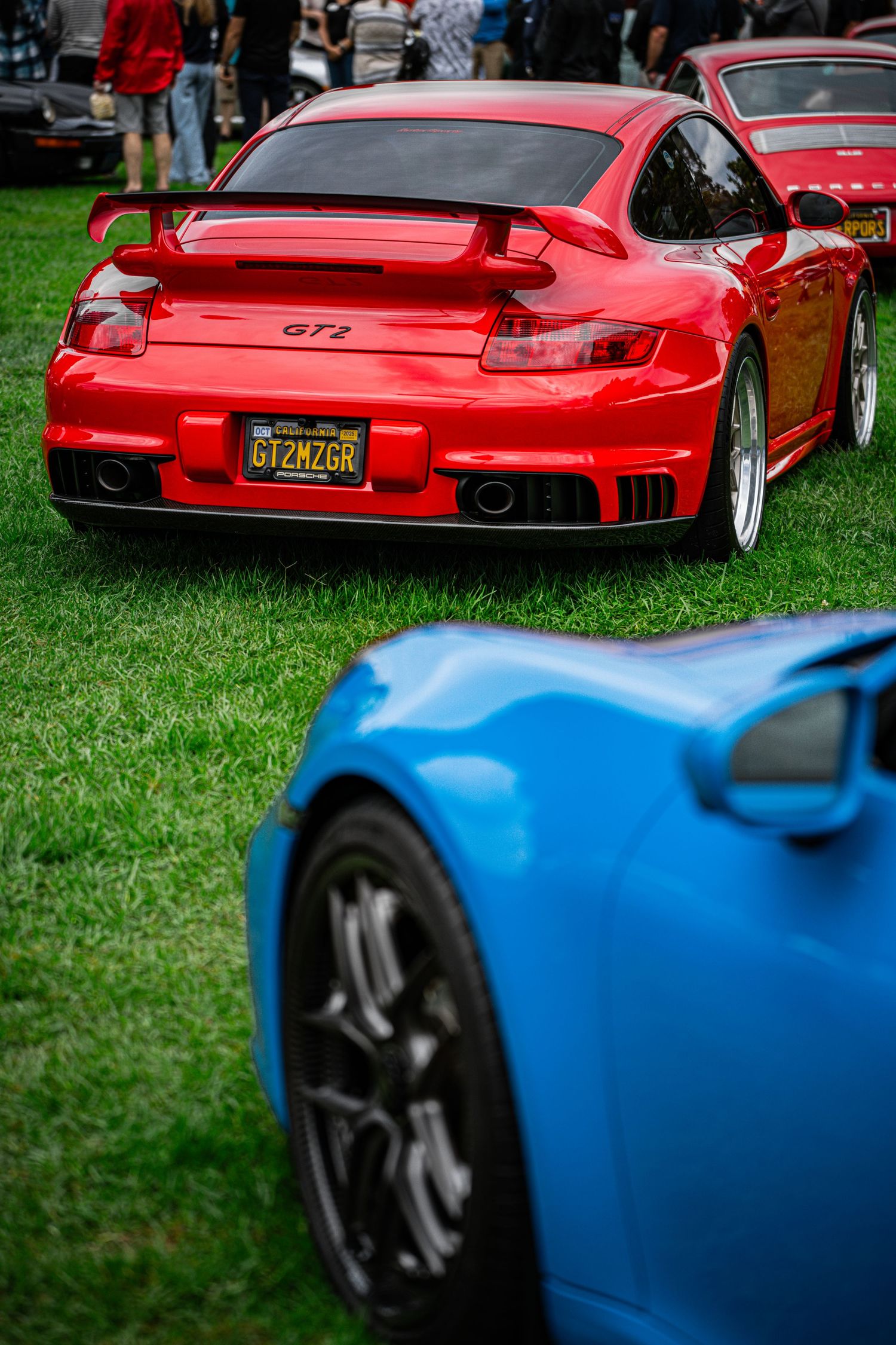 Red and blue Porsche sports cars lined up on grass at a car show.