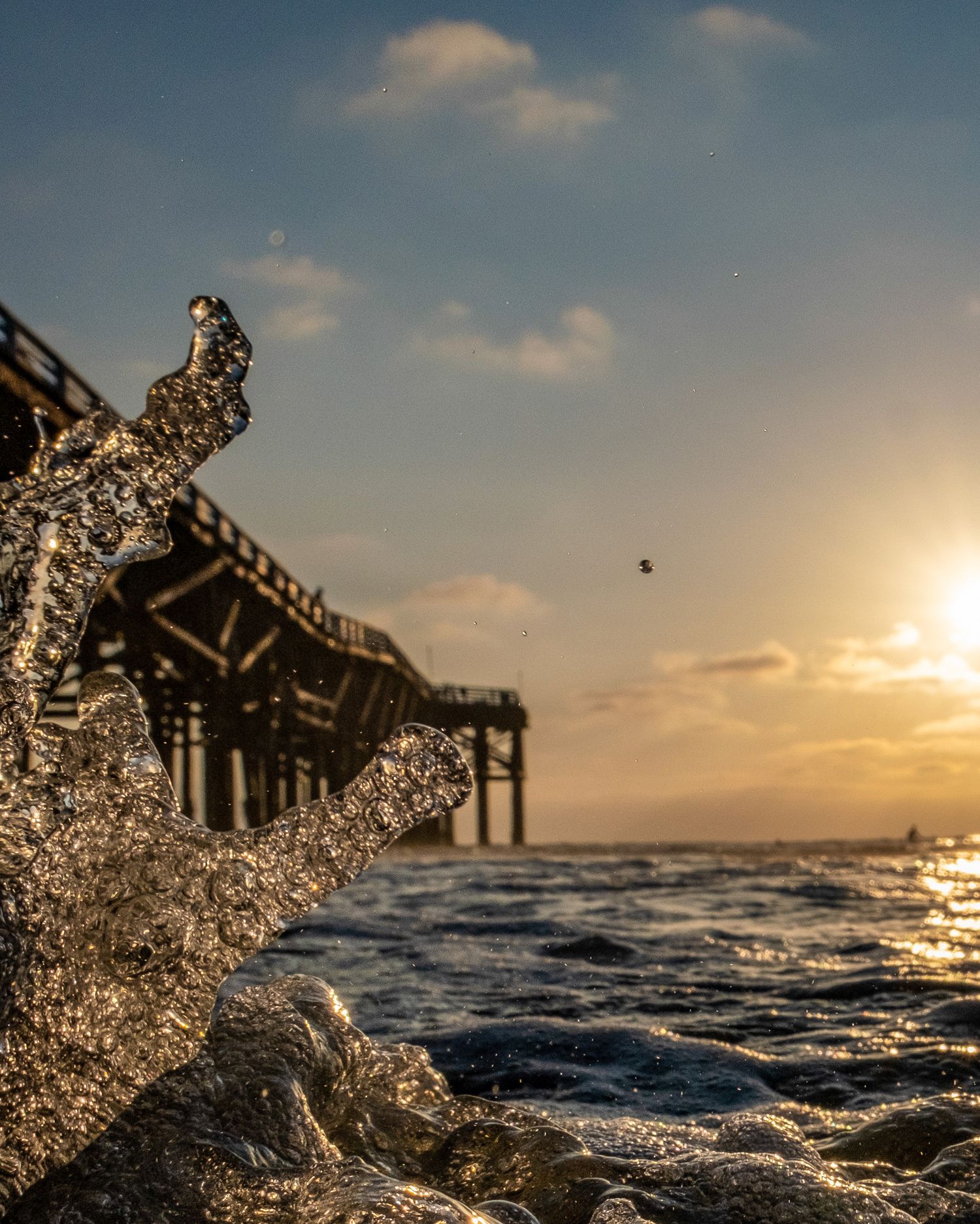 Golden sunset over ocean waves with silhouetted pier structure in the background.