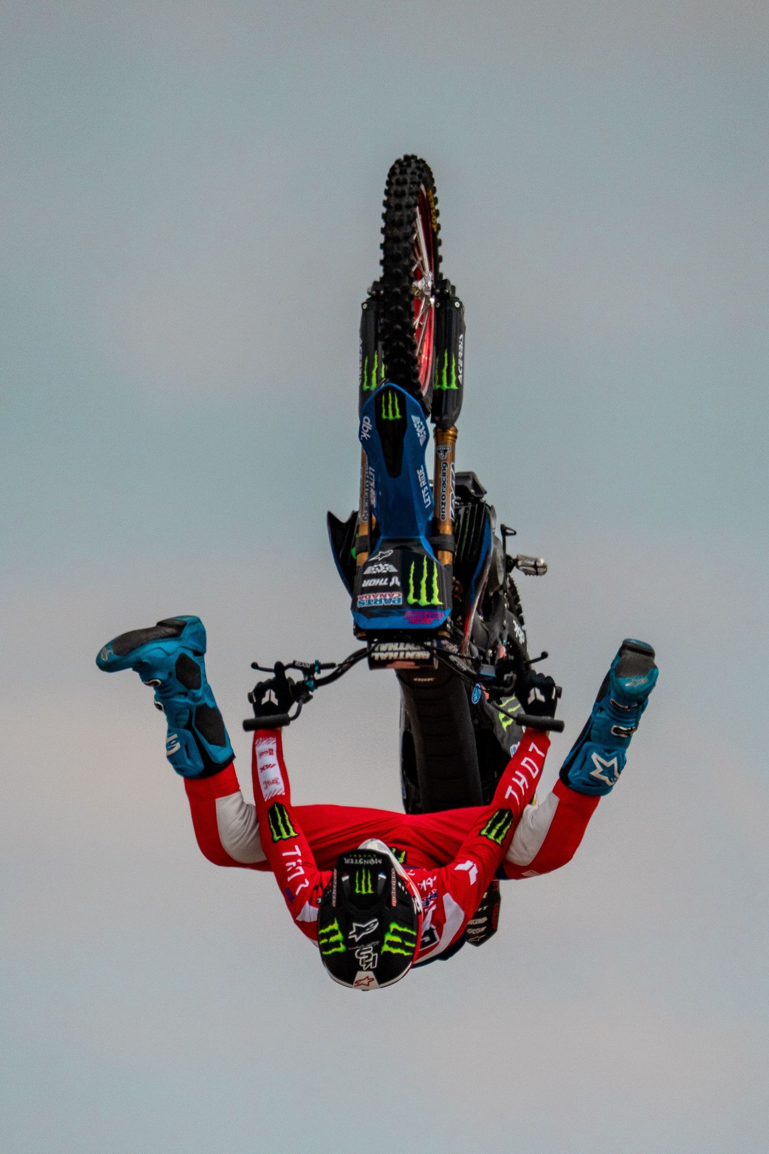 Extreme sports athlete performing an inverted aerial trick on a dirt bike against blue sky.