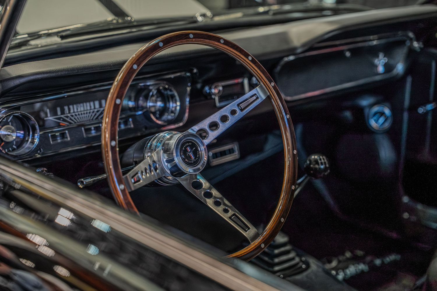 Vintage Ford Mustang interior featuring a classic wood-grain steering wheel, chrome accents, and retro dashboard gauges.