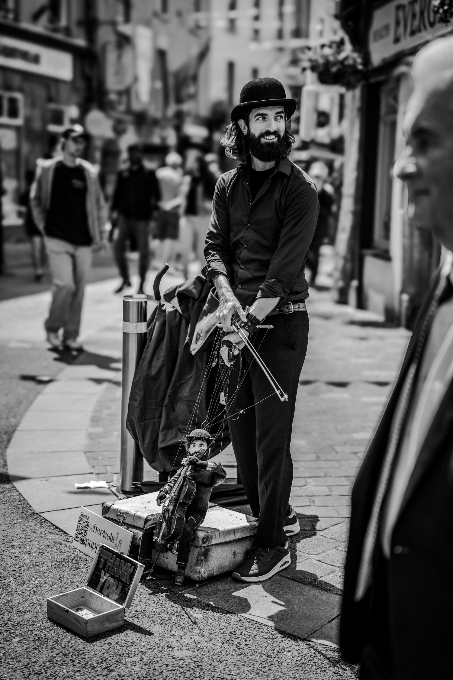 Black and white street photo of performer with instrument case on urban sidewalk.