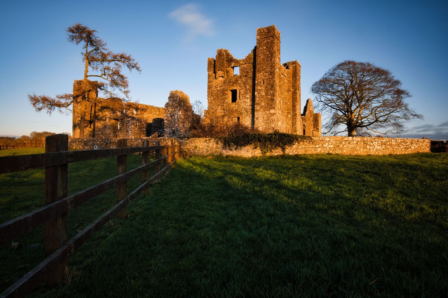 Ancient castle ruins silhouetted against blue sky at sunset with stone walls and towers.