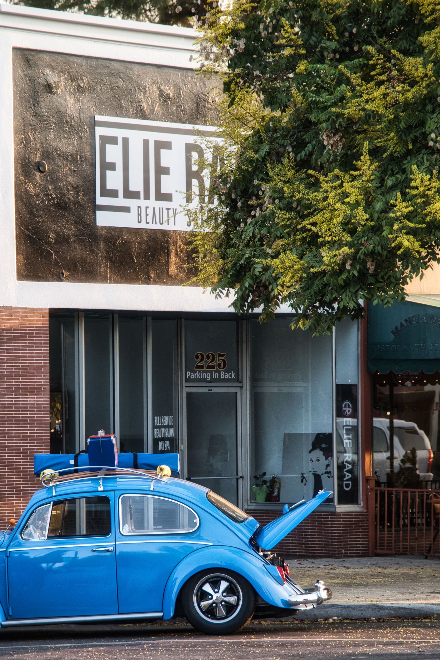 Blue vintage Volkswagen Beetle cars lined up outside a brick storefront.