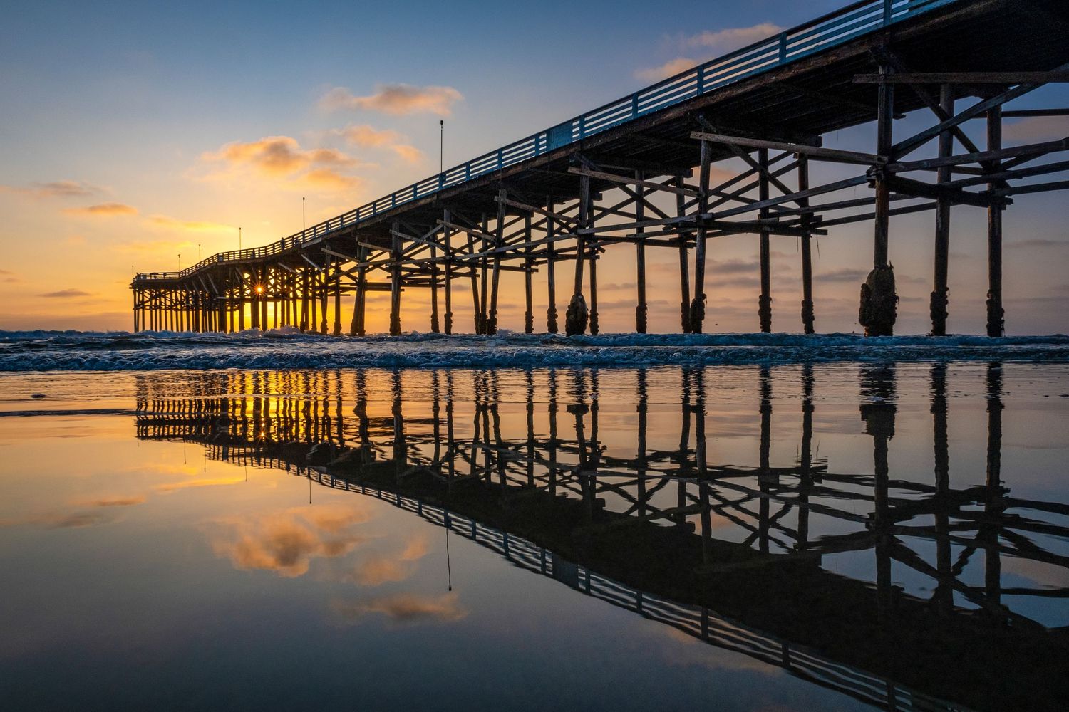 Wooden pier silhouetted against a colorful sunset with perfect reflections in calm water.