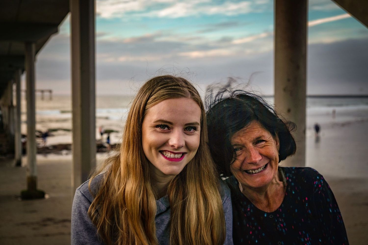 Candid beach portraits captured under a pier during sunset.
