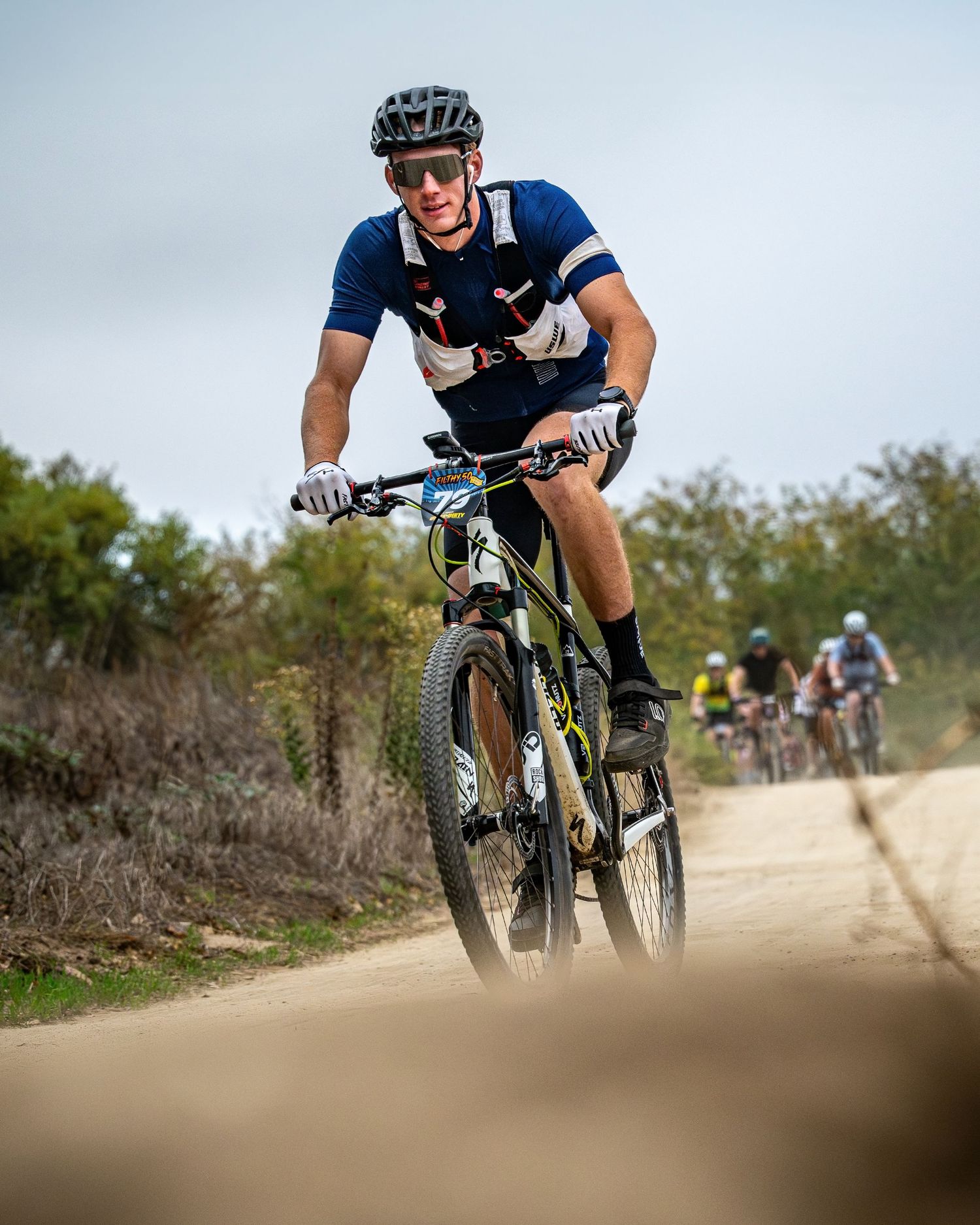 Mountain biker riding on a dusty trail during a race competition.