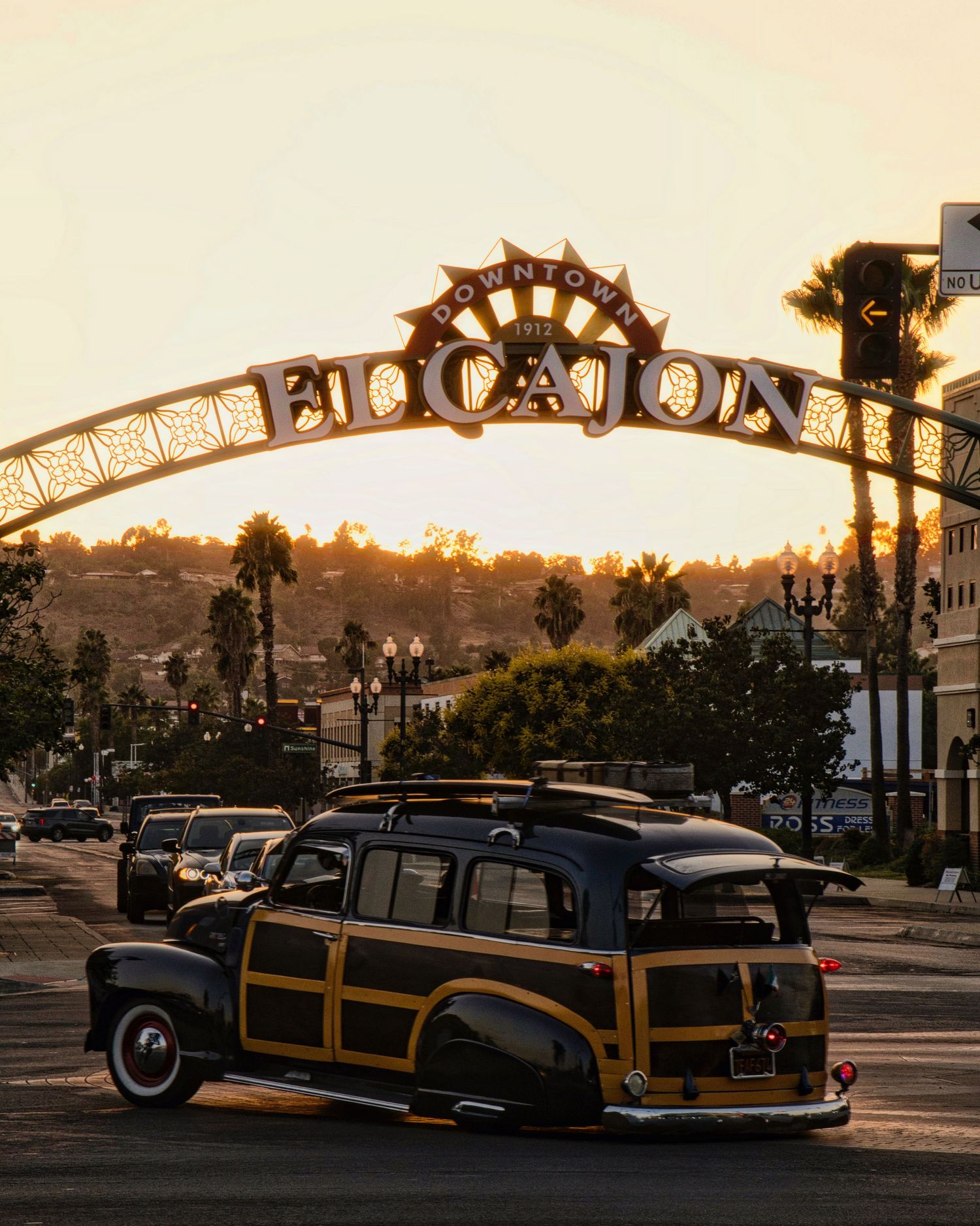 Classic wooden station wagon parked under a vintage entrance arch during golden sunset.