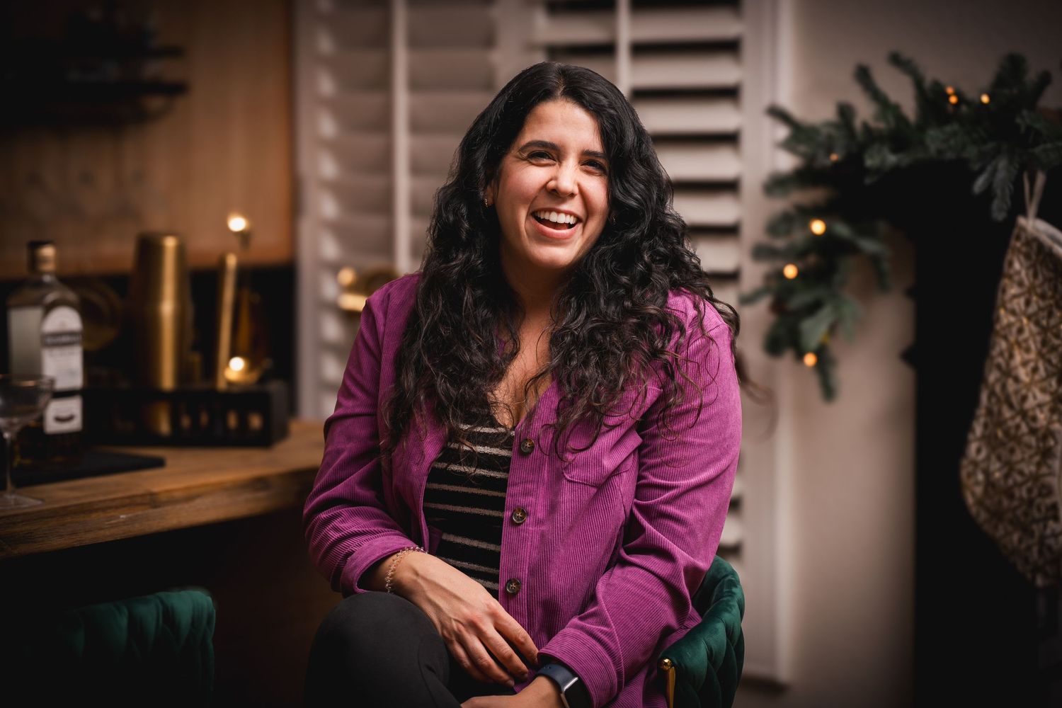 Professional lifestyle photo of someone in a vibrant purple blazer sitting in a warmly lit room with window shutters.