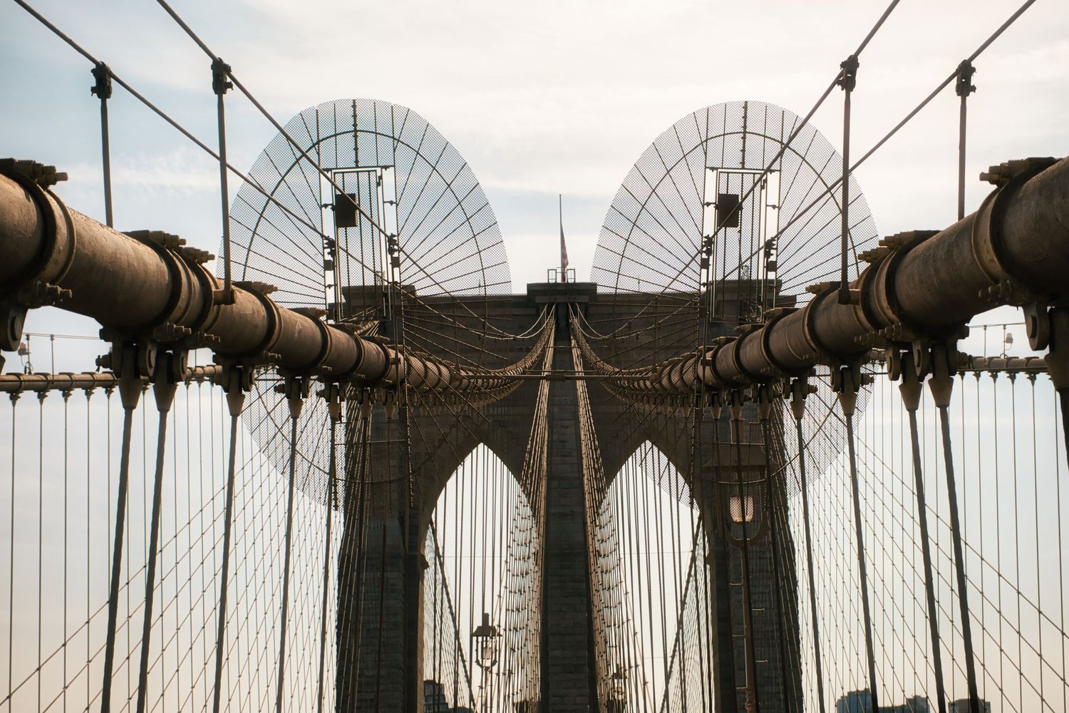 Architectural detail of Brooklyn Bridge cables and supports against an overcast sky.