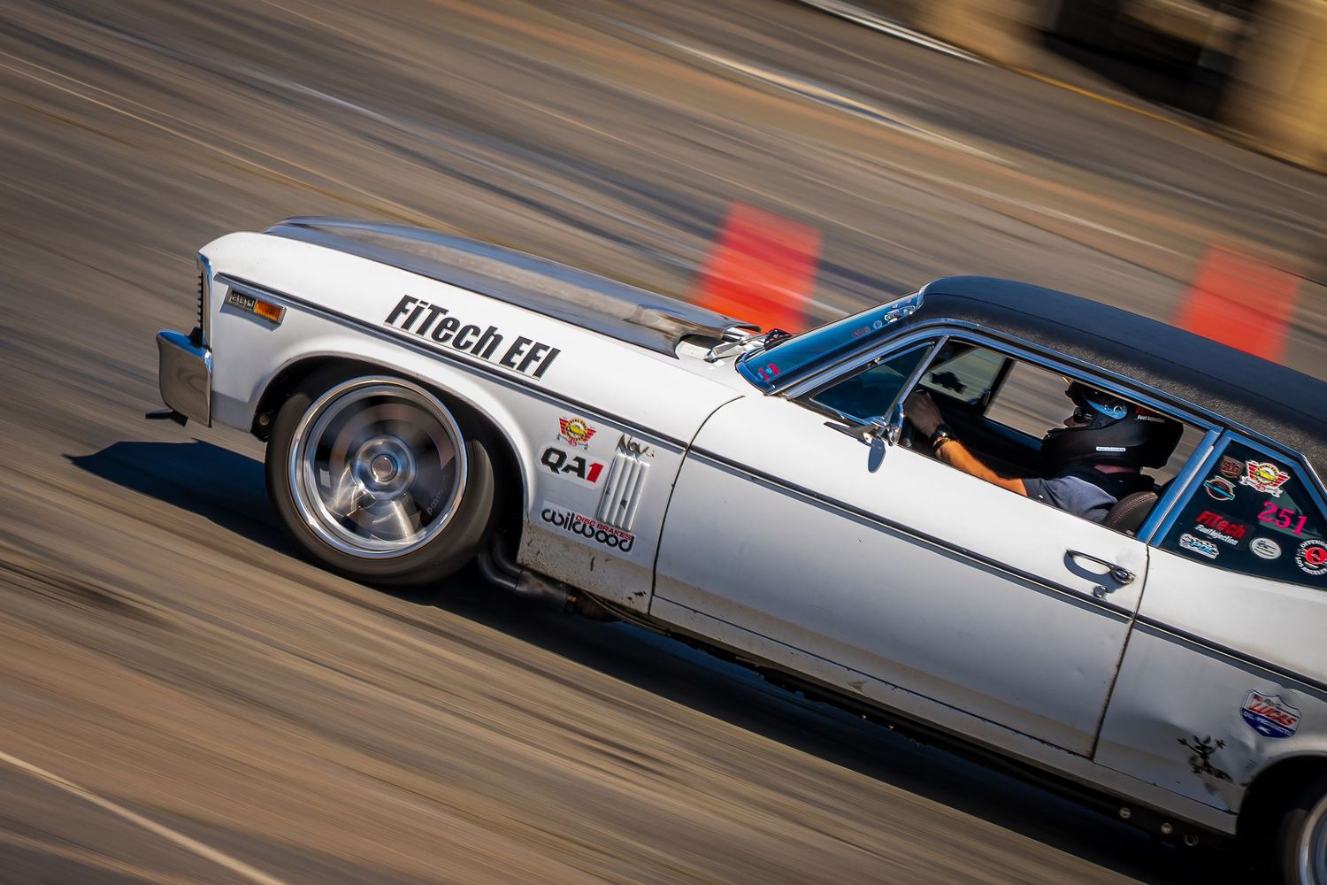 White FiTech EFI classic car racing on a track at high speed, with motion blur in the background.