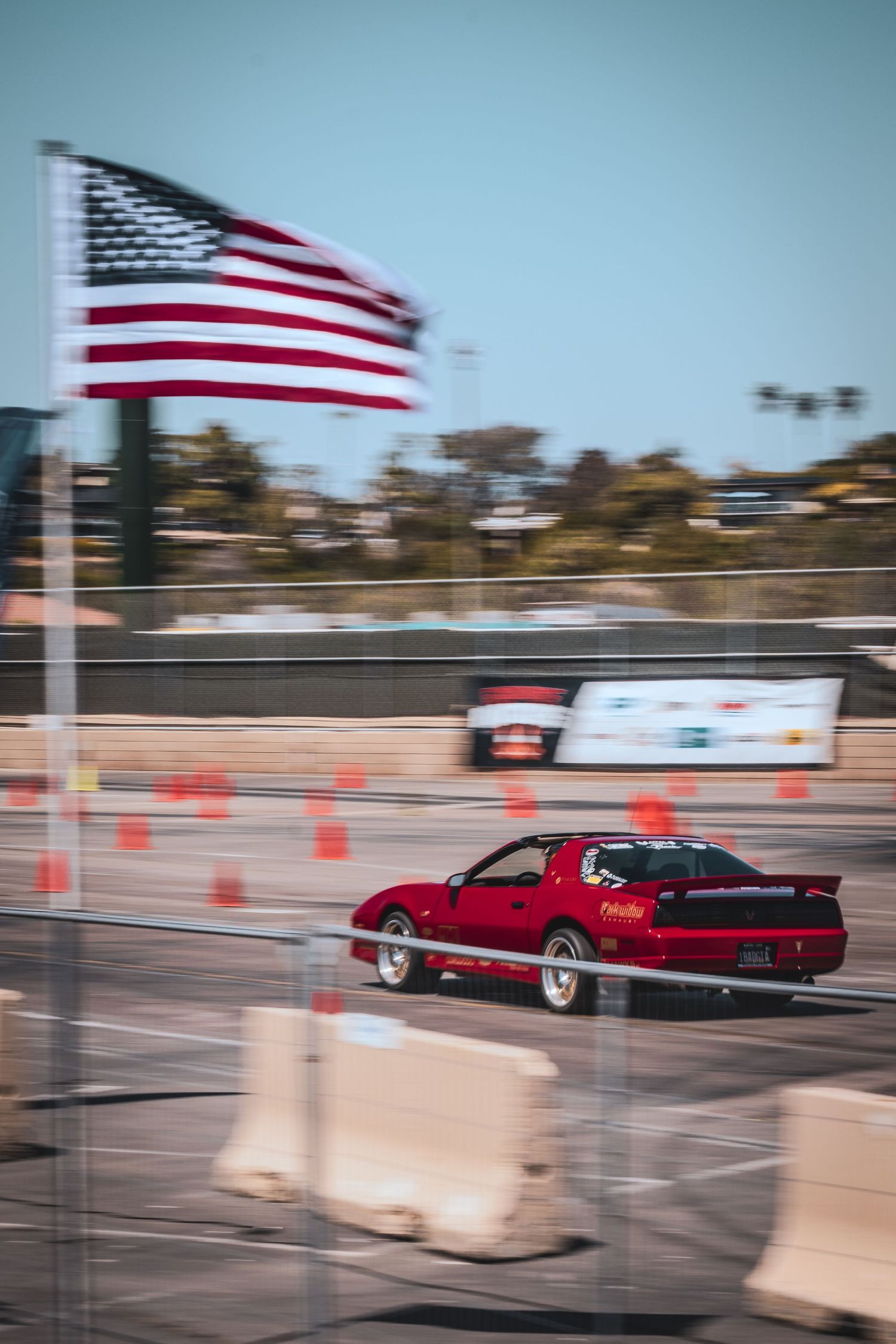 Red sports car drifting on track with American flag waving in background.