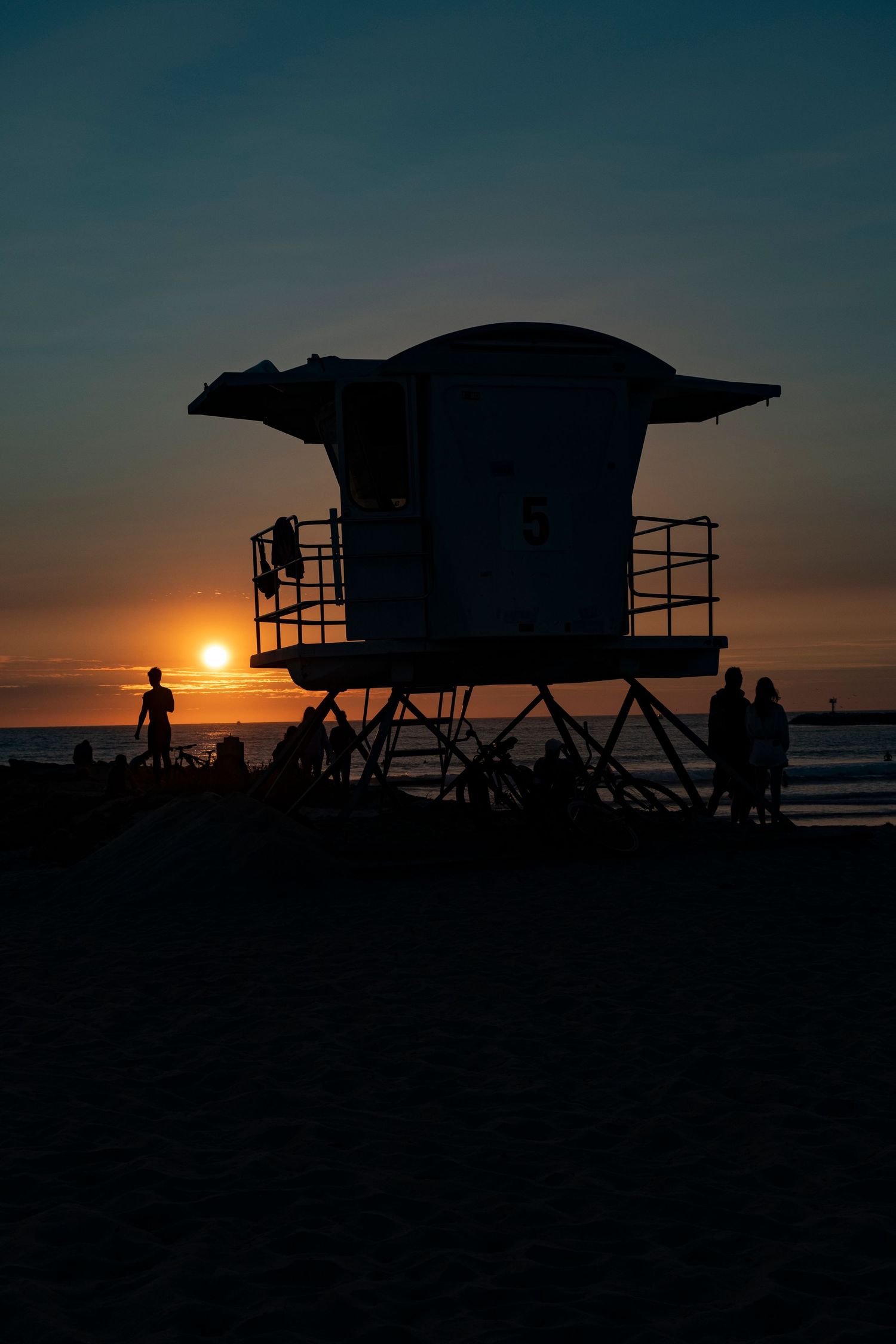 Silhouettes of lifeguard towers on beach at sunset with orange sky.