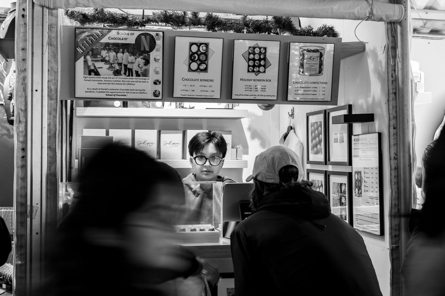 Black and white photo of food vendor stall with customers in motion blur.