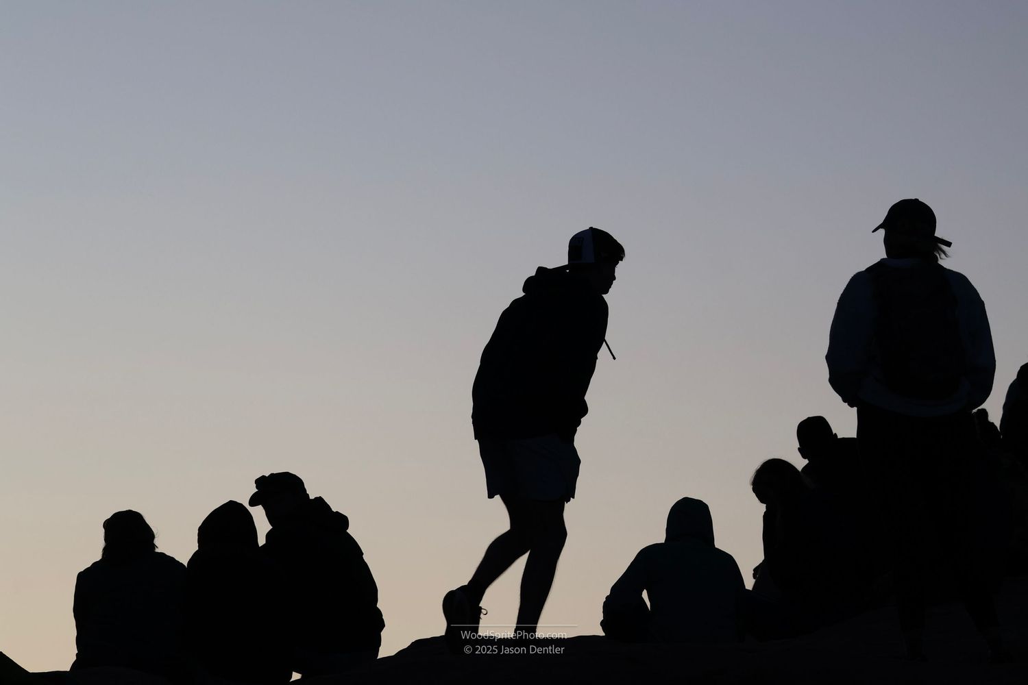Silhouette of several people standing on a rocky outcrop against an early morning sky. One person is walking away from the group.