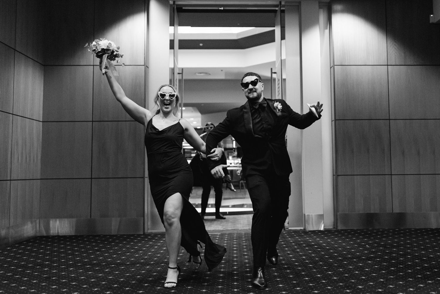Wedding party dancing and celebrating in black and white in hotel hallway.