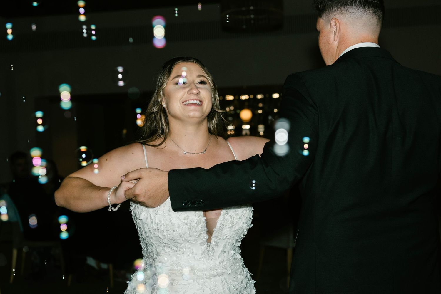 Bride in a beaded gown shares first dance with groom surrounded by floating bubbles at wedding reception.