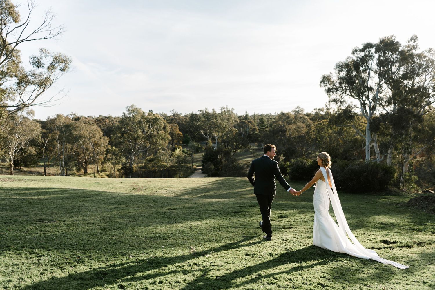 A couple walks together on a grassy hillside during a scenic outdoor wedding photo session.