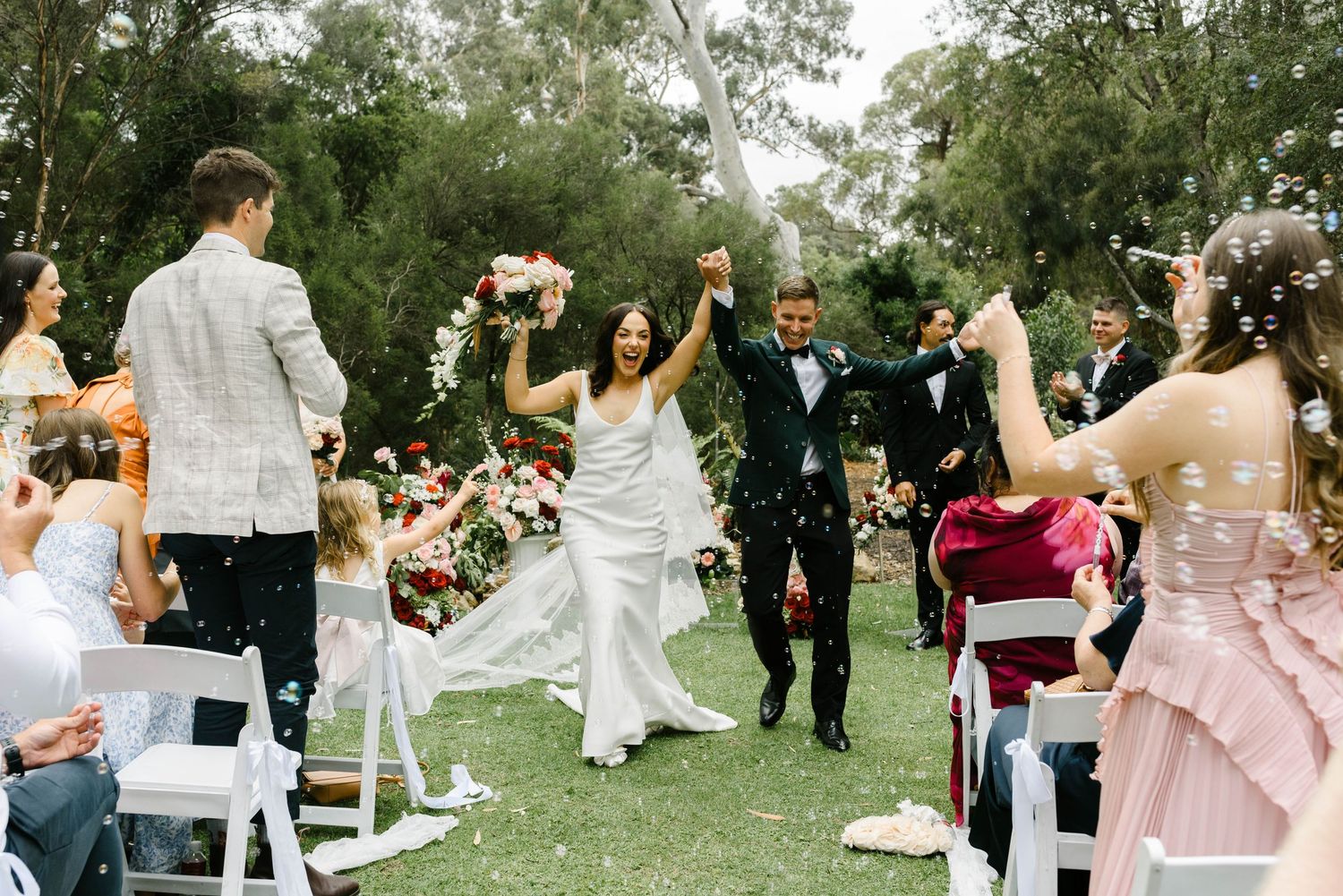 Wedding party dances together in a line during outdoor garden reception celebration.