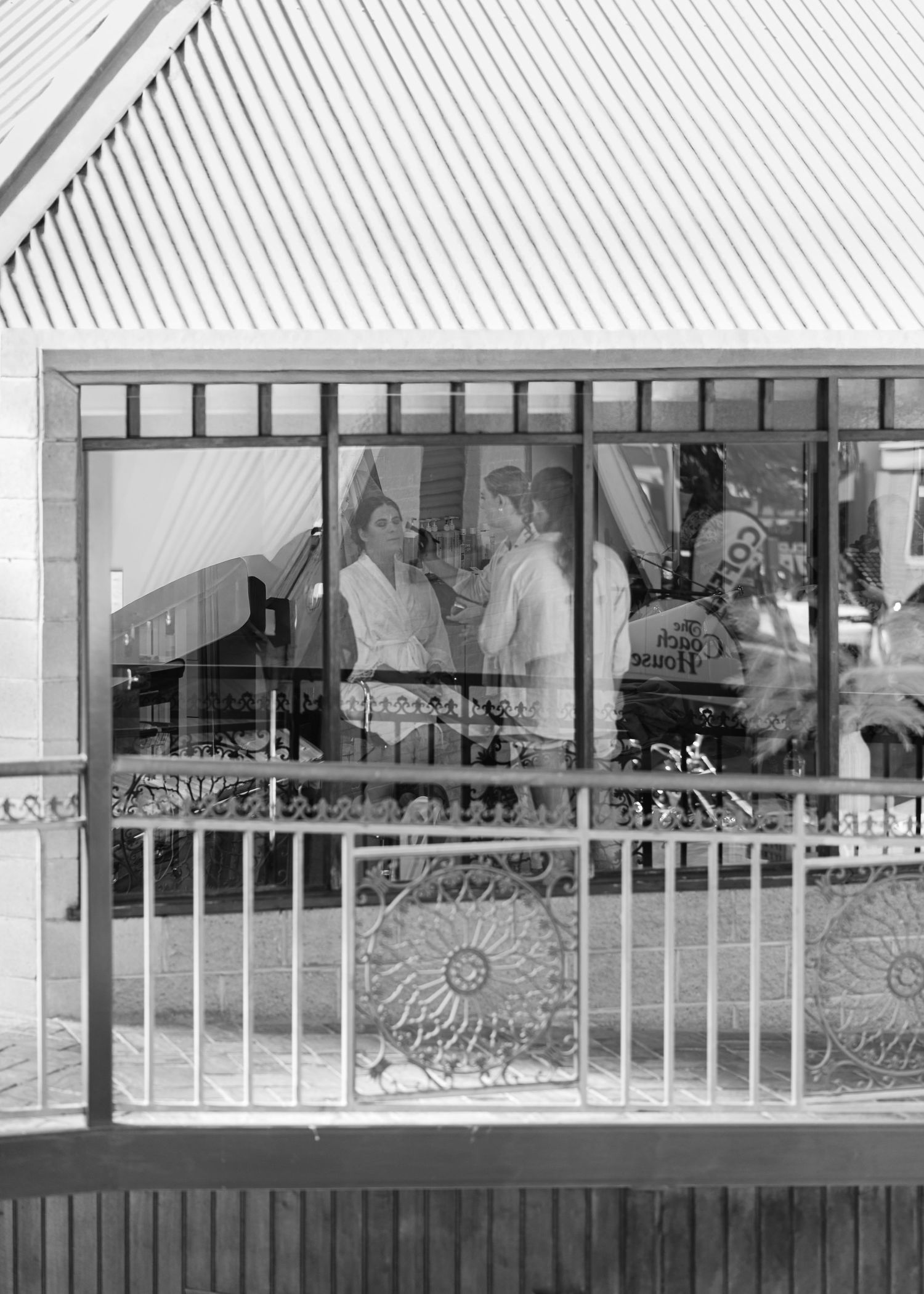 Black and white photo of people reflected in a shop window with decorative iron railing in foreground.