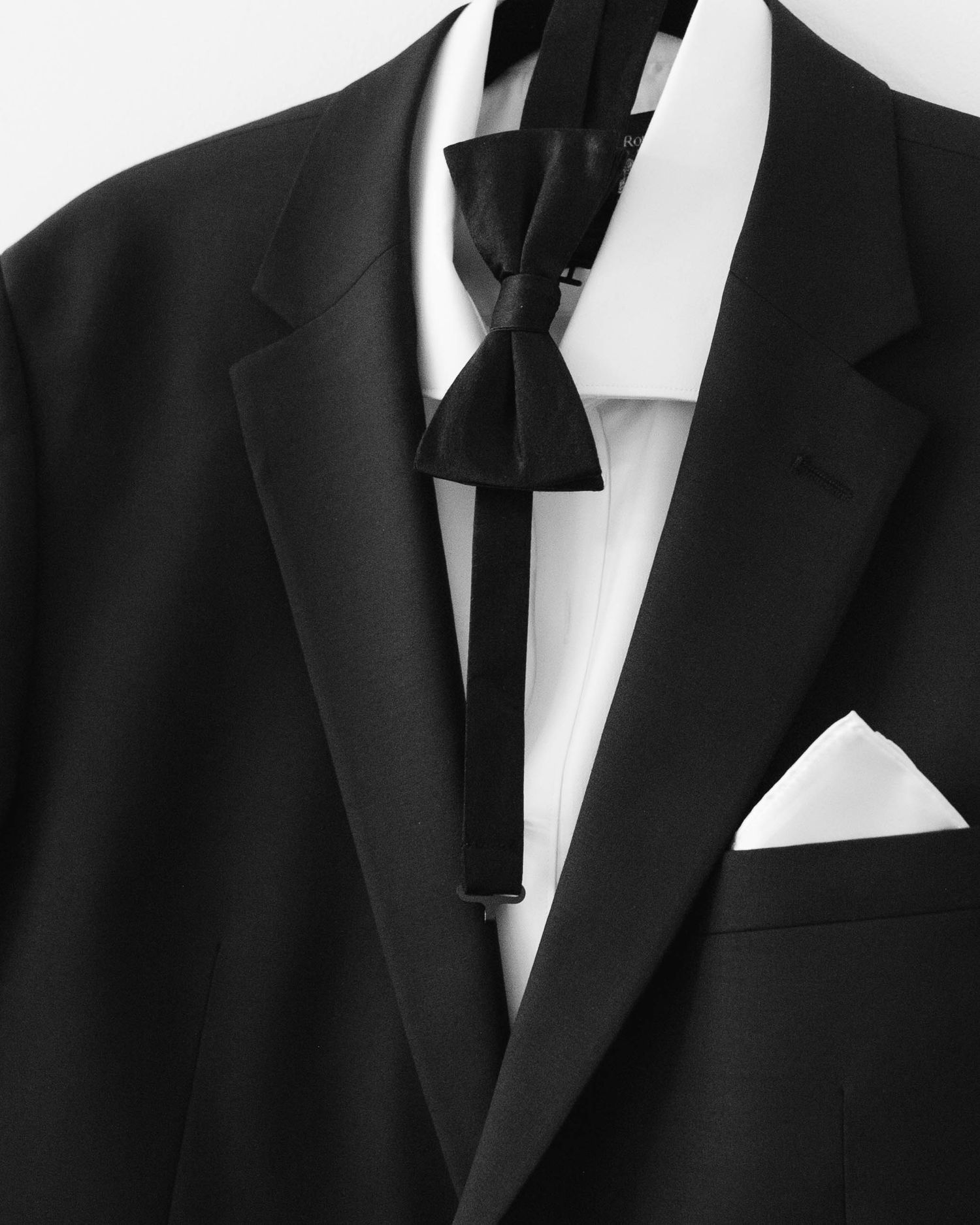 A row of black tuxedo jackets and white dress shirts displayed on hangers against a white background.