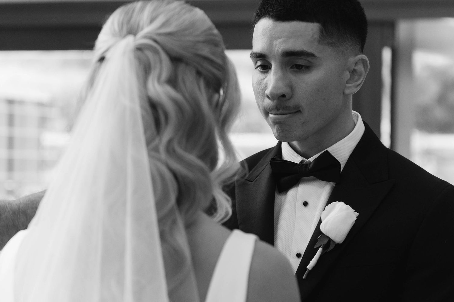 Black and white wedding photo of groom in tuxedo sharing an emotional moment with bride in white dress.