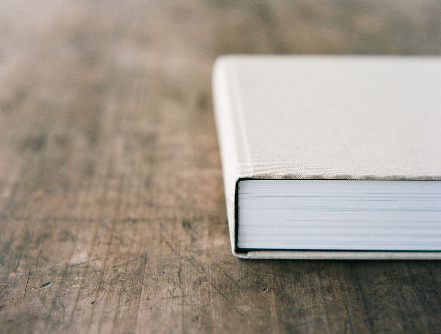 Close-up view of hardcover books stacked on a weathered wooden surface with shallow depth of field.