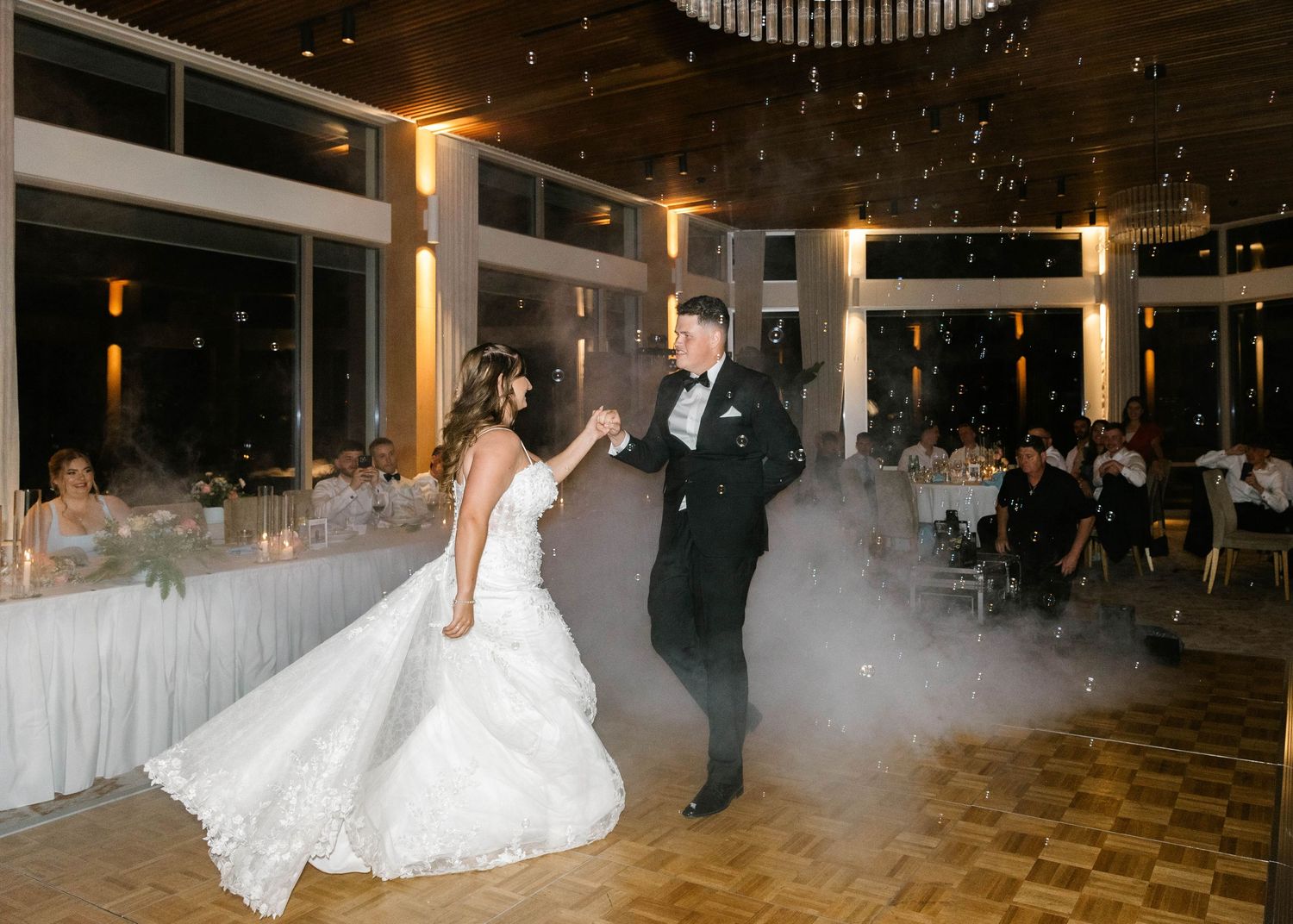 Bride and groom share first dance on foggy dance floor at elegant wedding reception venue.
