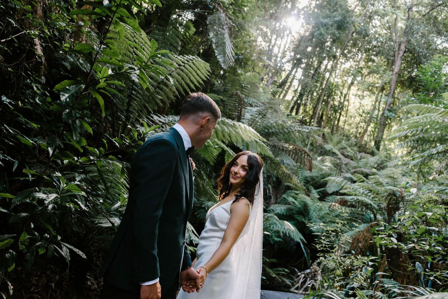 A couple shares an intimate moment surrounded by lush ferns and greenery in a forest setting.