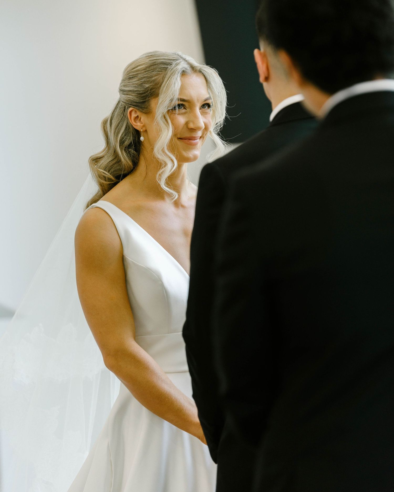 Bride in white v-neck gown smiling at groom during wedding ceremony.