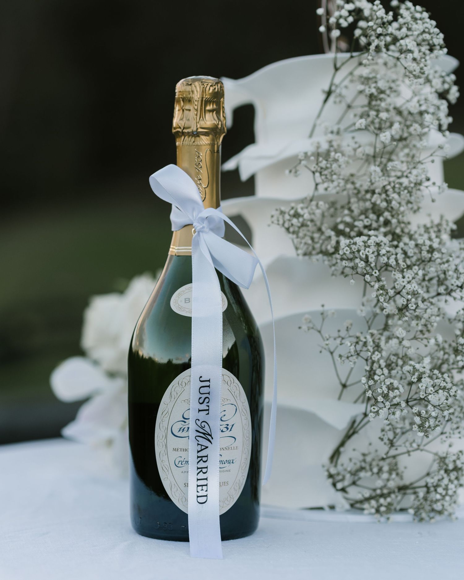 Champagne bottle with a white ribbon reading Just Married, beside baby's breath and white floral decor on a wedding table.