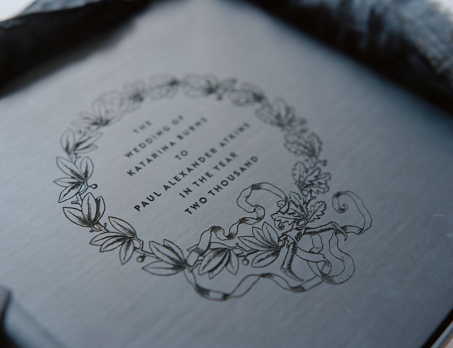 Elegant dark wedding invitation with floral wreath design featuring delicate botanical illustrations in silver ink.