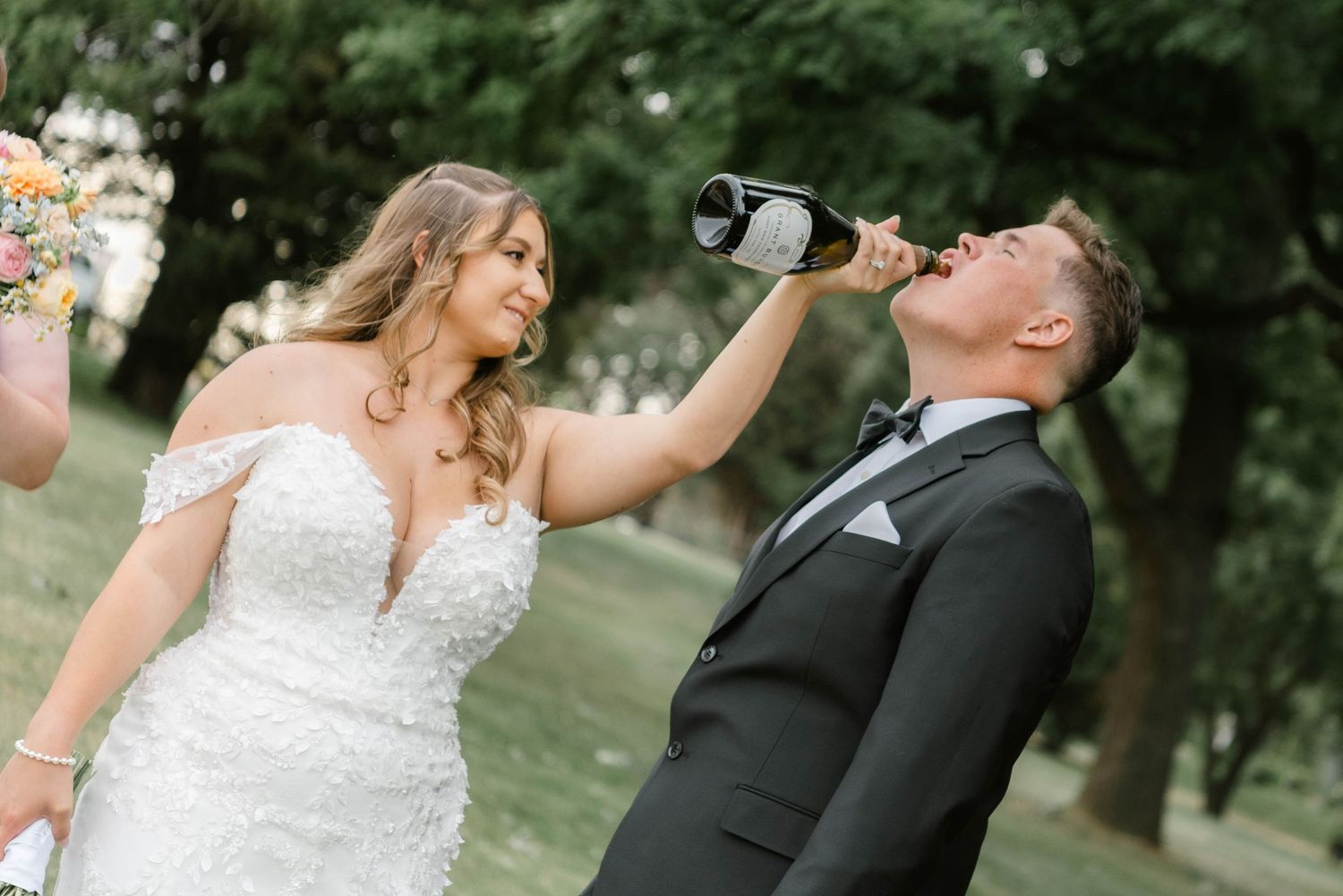Bride and groom in formal wedding attire taking celebratory shots together in an outdoor garden setting.