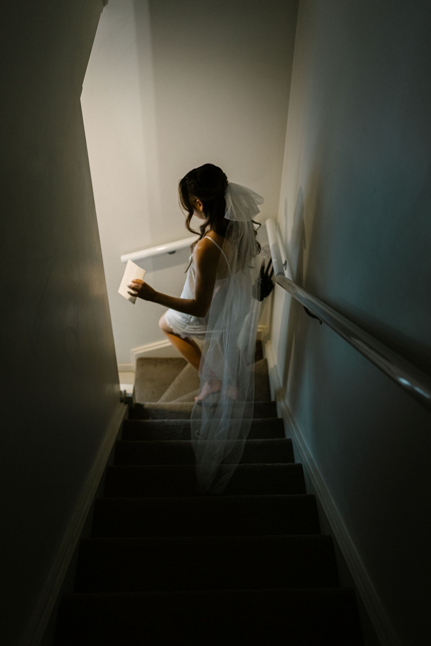 Atmospheric shot of bride descending dimly lit staircase in flowing white dress.