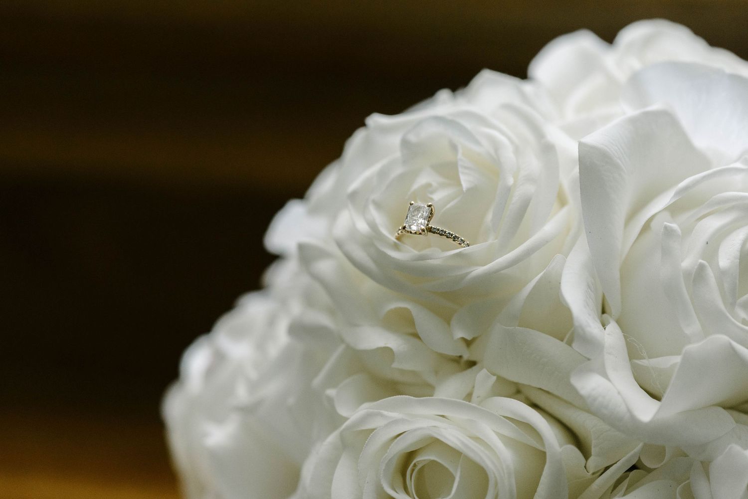 Gold diamond engagement ring nestled among white roses in a bridal bouquet.