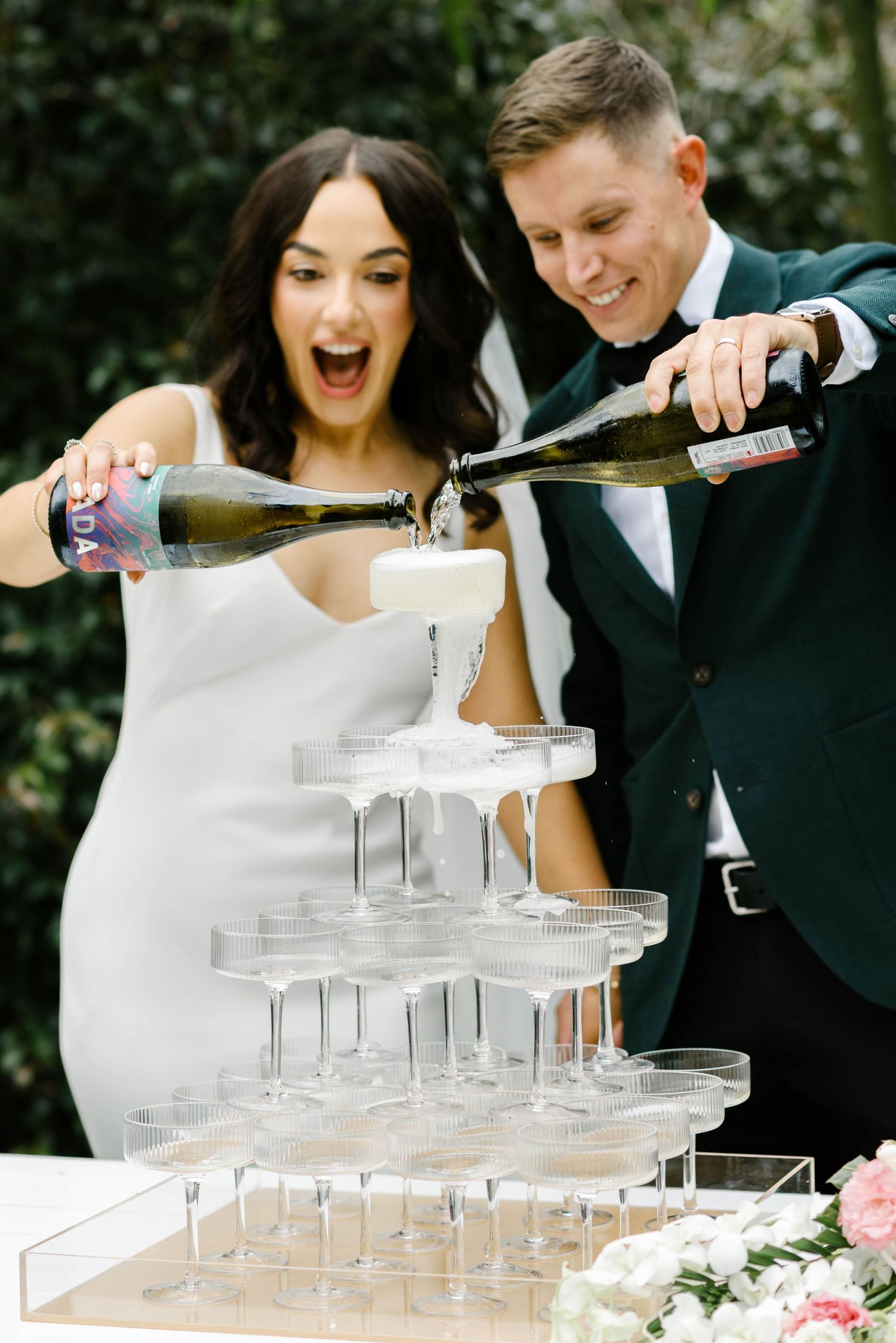A couple pours champagne into a tower of glasses at their wedding celebration, creating a festive cascade effect.