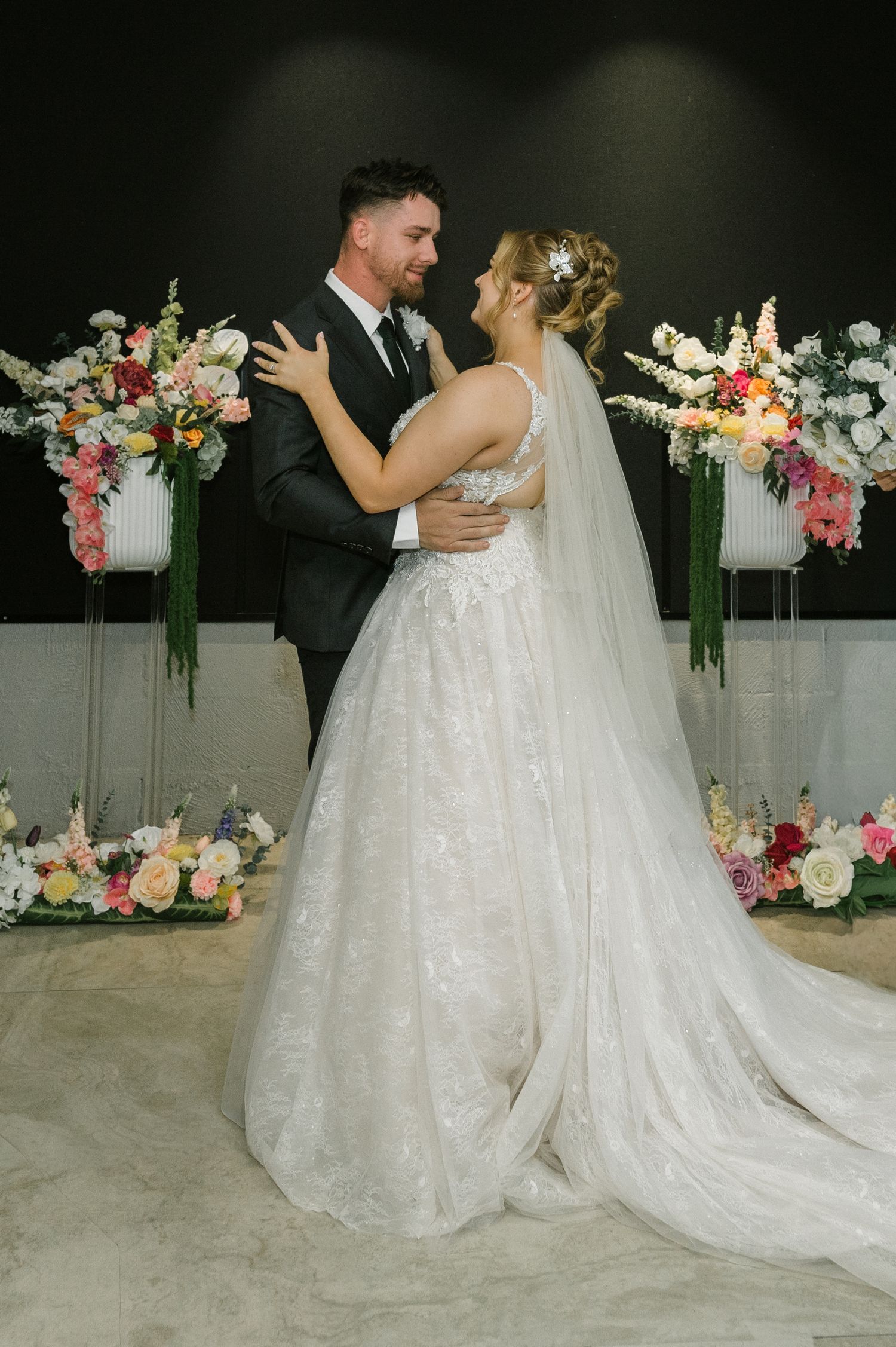 Bride and groom share a romantic first dance embrace surrounded by colorful floral arrangements at their wedding ceremony.