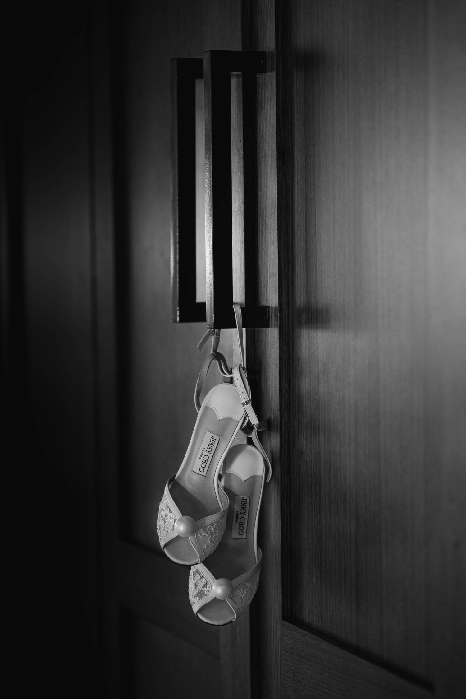 Elegant white bridal heels hanging dramatically against a dark wooden wall in a sequence.