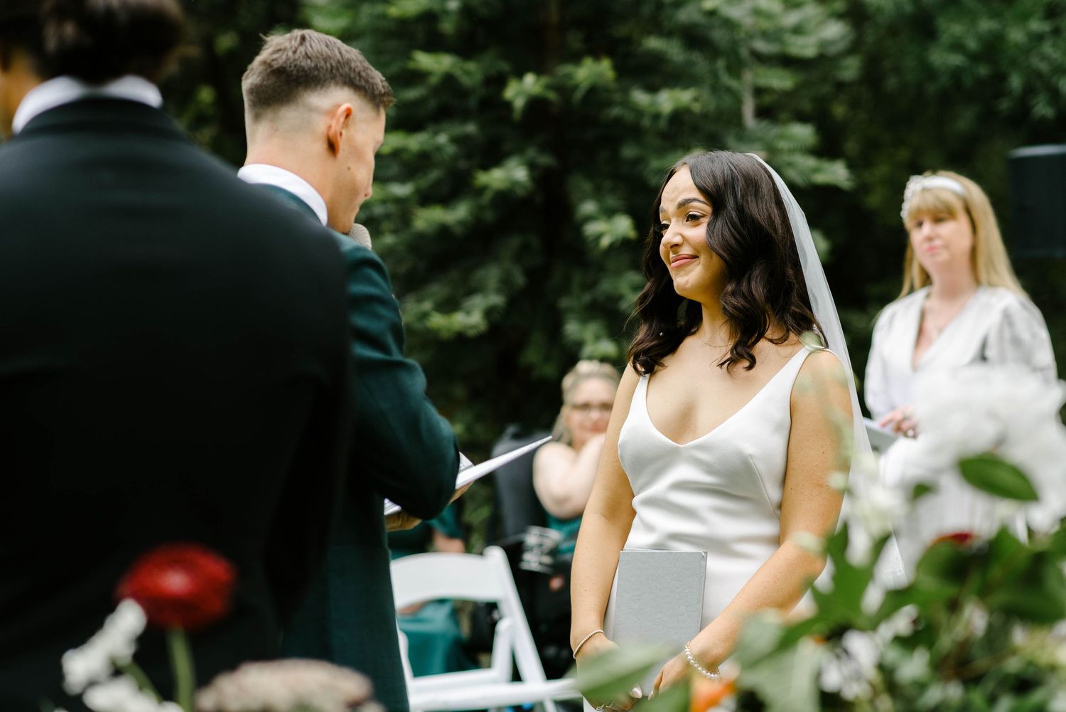 Wedding guests enjoy outdoor reception with drinks and conversation at tables surrounded by lush greenery.