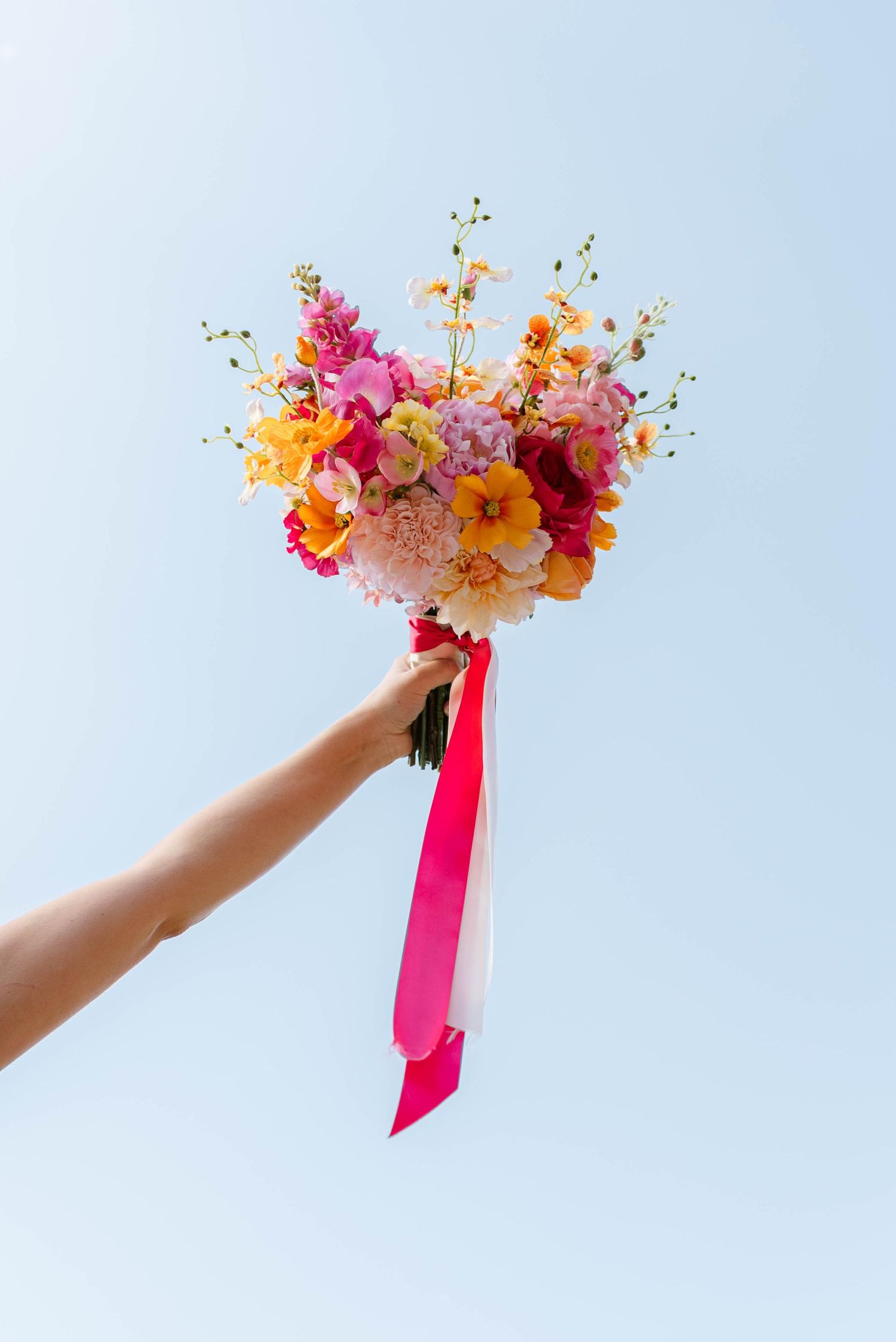 Three sequential shots of a hand holding a vibrant bouquet with pink and orange flowers against a light blue sky background.