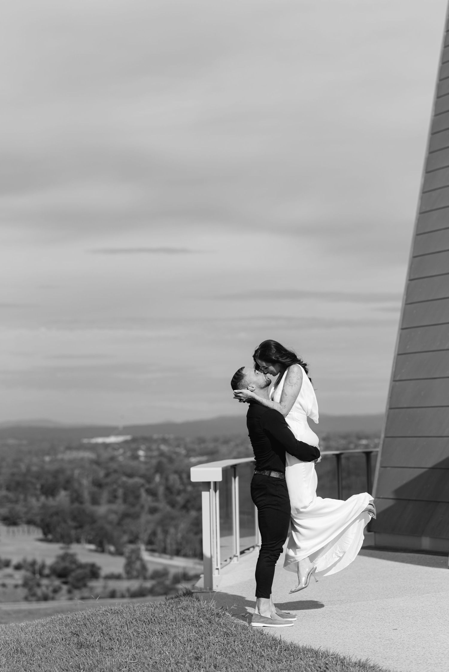 A person in white sits contemplatively on a rooftop overlooking a scenic landscape.
