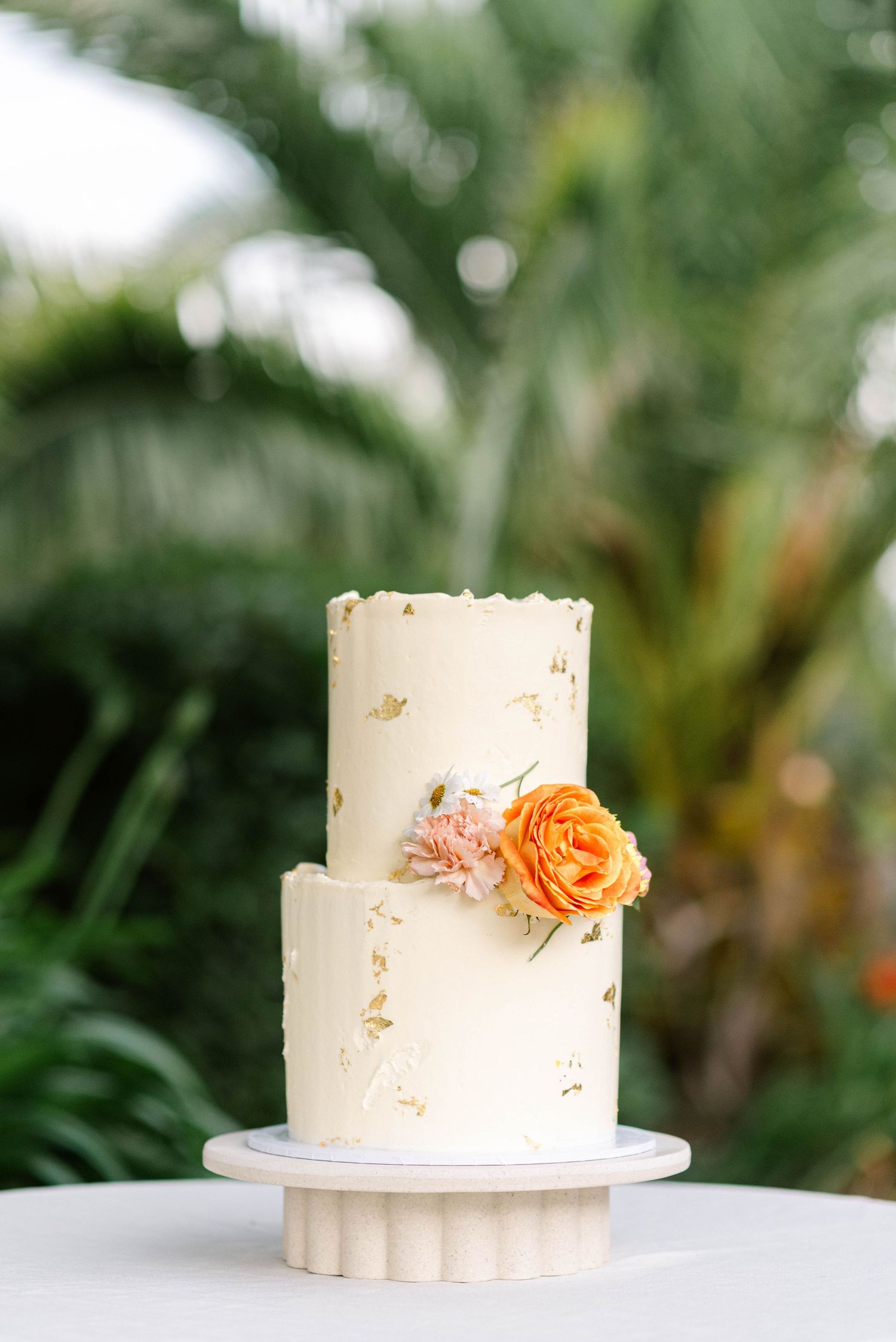 A series of four white wedding cakes with delicate peach floral decorations displayed against a blurred green background.