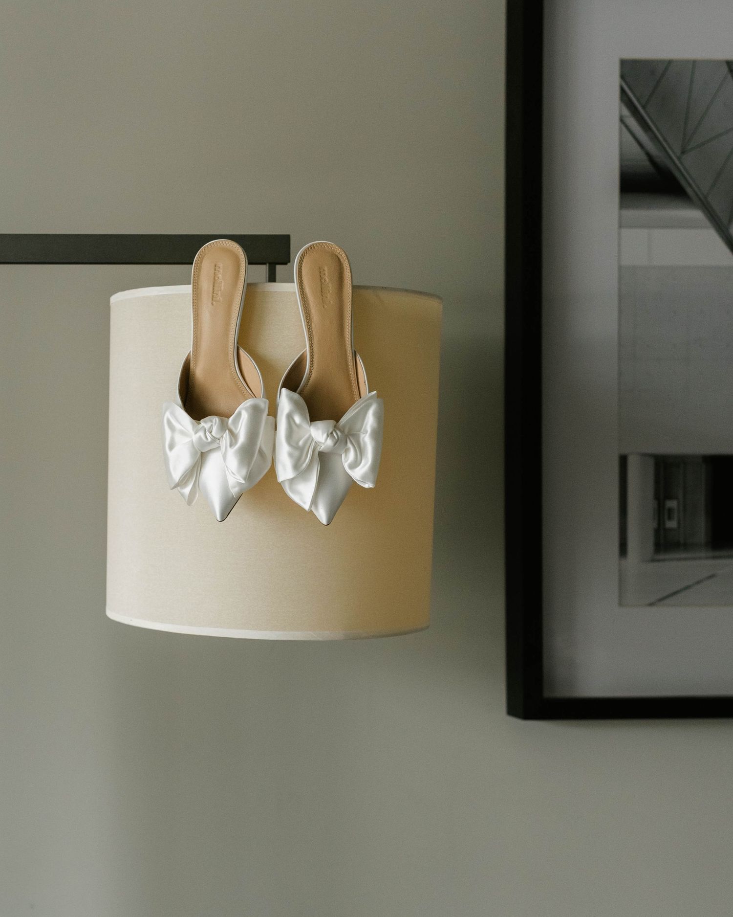 A decorative silver bow accent adorns a tan lampshade mounted on a wall against a neutral background.