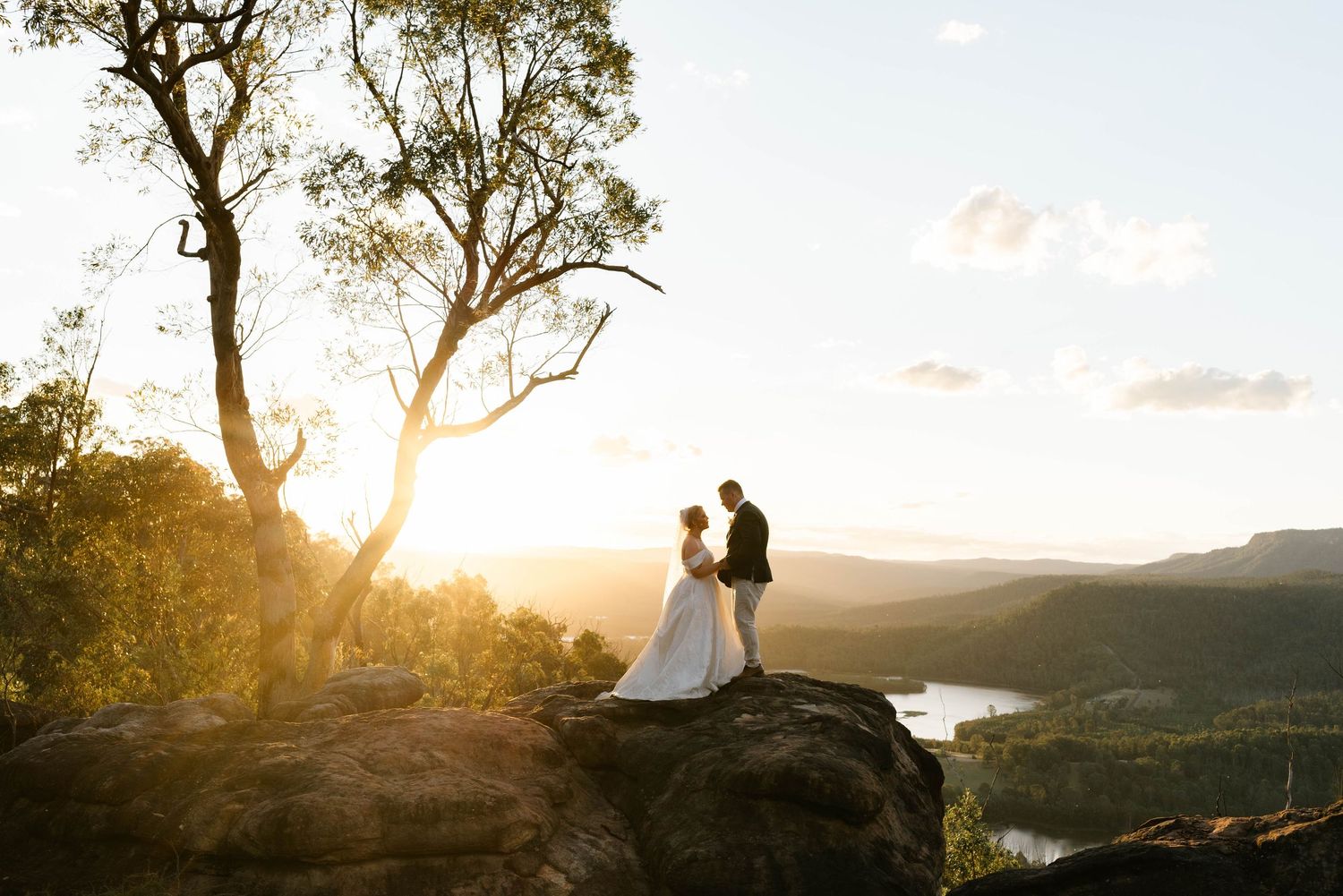 A couple shares a romantic moment at sunset overlooking a scenic mountain landscape.
