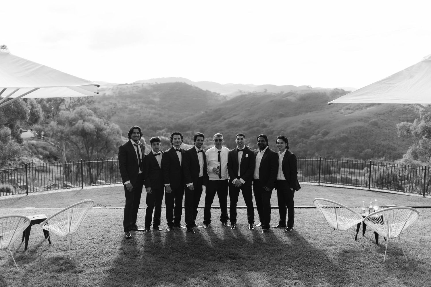 Black and white photo of groom and groomsmen posing outdoors at a hillside wedding venue.