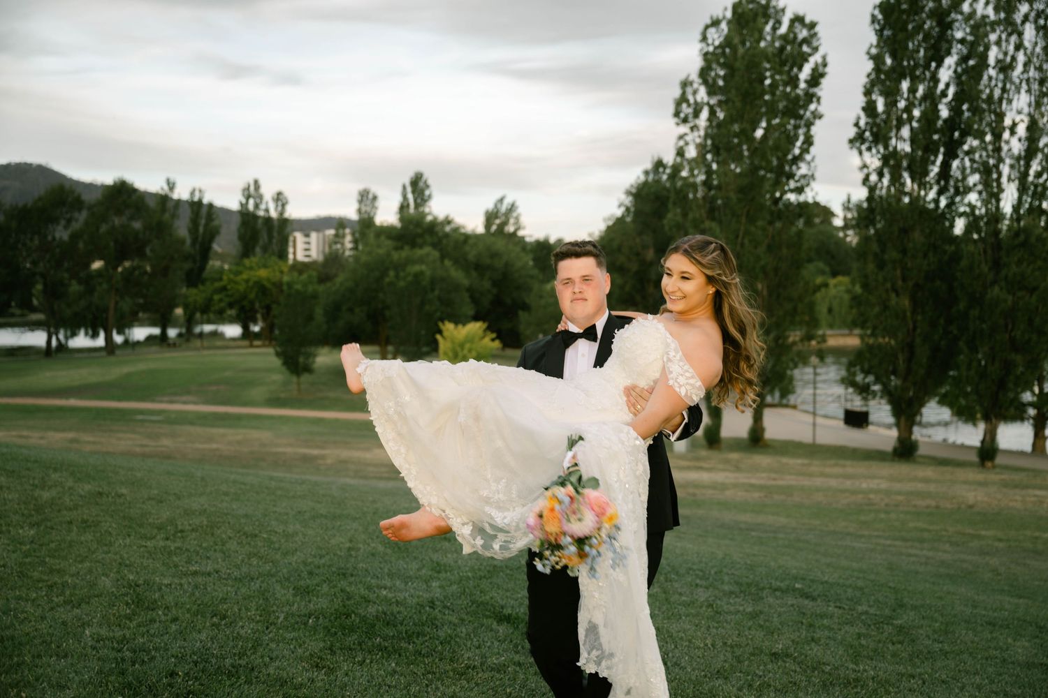 A couple in wedding attire shares a romantic moment on a lush green lawn during their outdoor celebration.