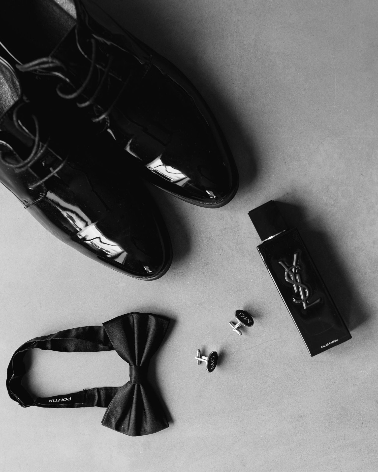 Artistically arranged black and white formal men's shoes and bow ties on a light background.