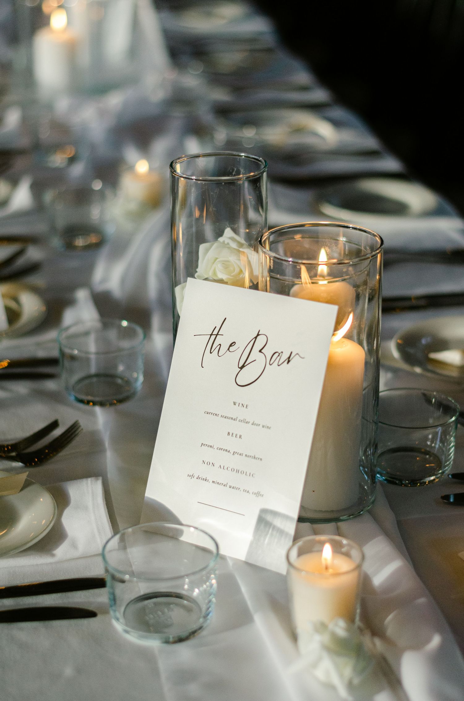 Elegant wedding reception table setting with glowing candles and name cards in soft lighting.