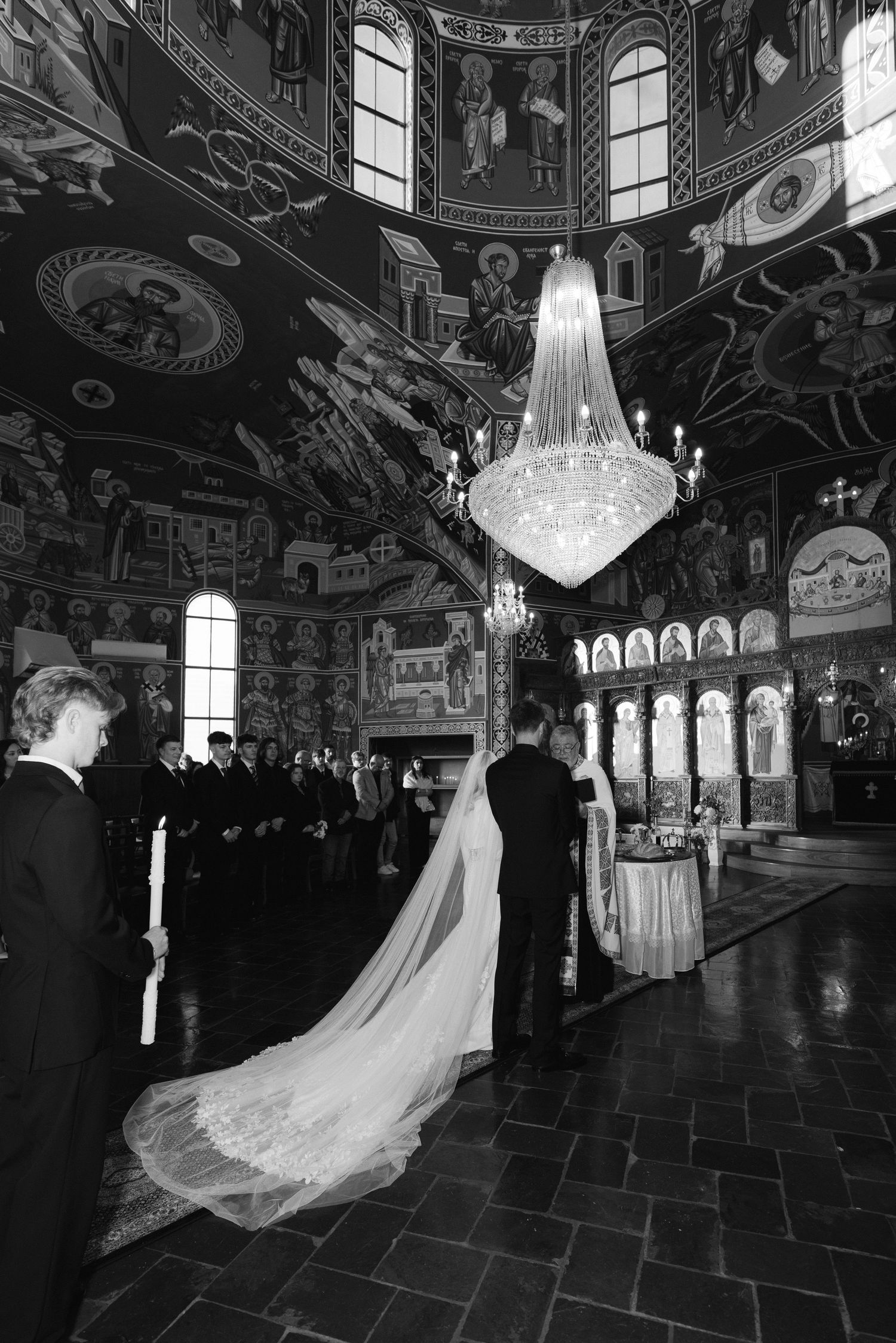 Black and white photo of a bride in a long veil during a wedding ceremony inside an ornate Orthodox church.
