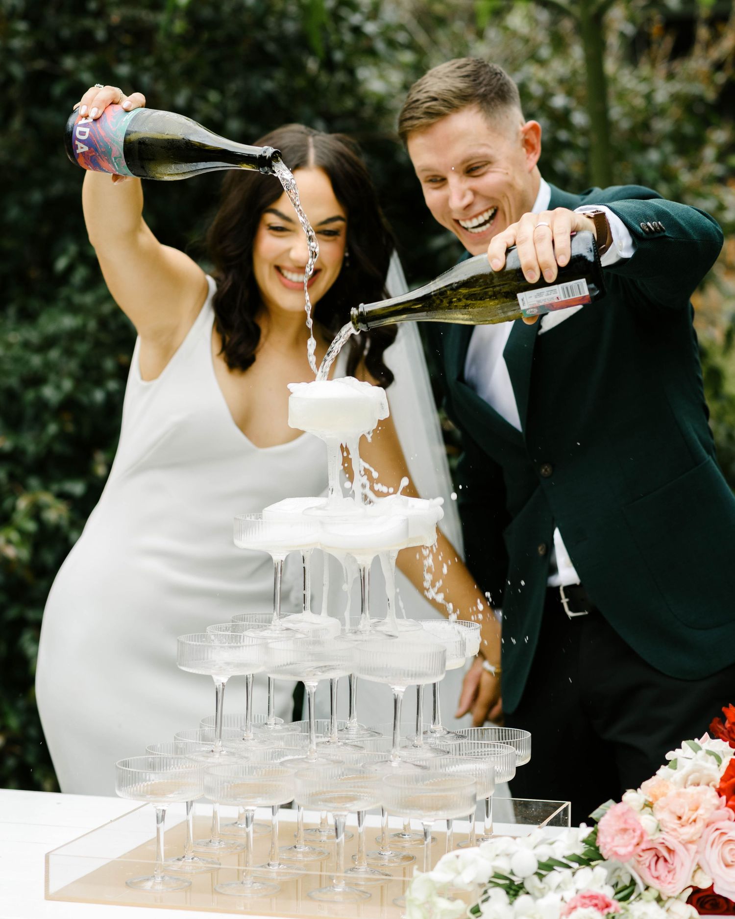 A couple pours champagne into a tower of glasses during their wedding celebration.