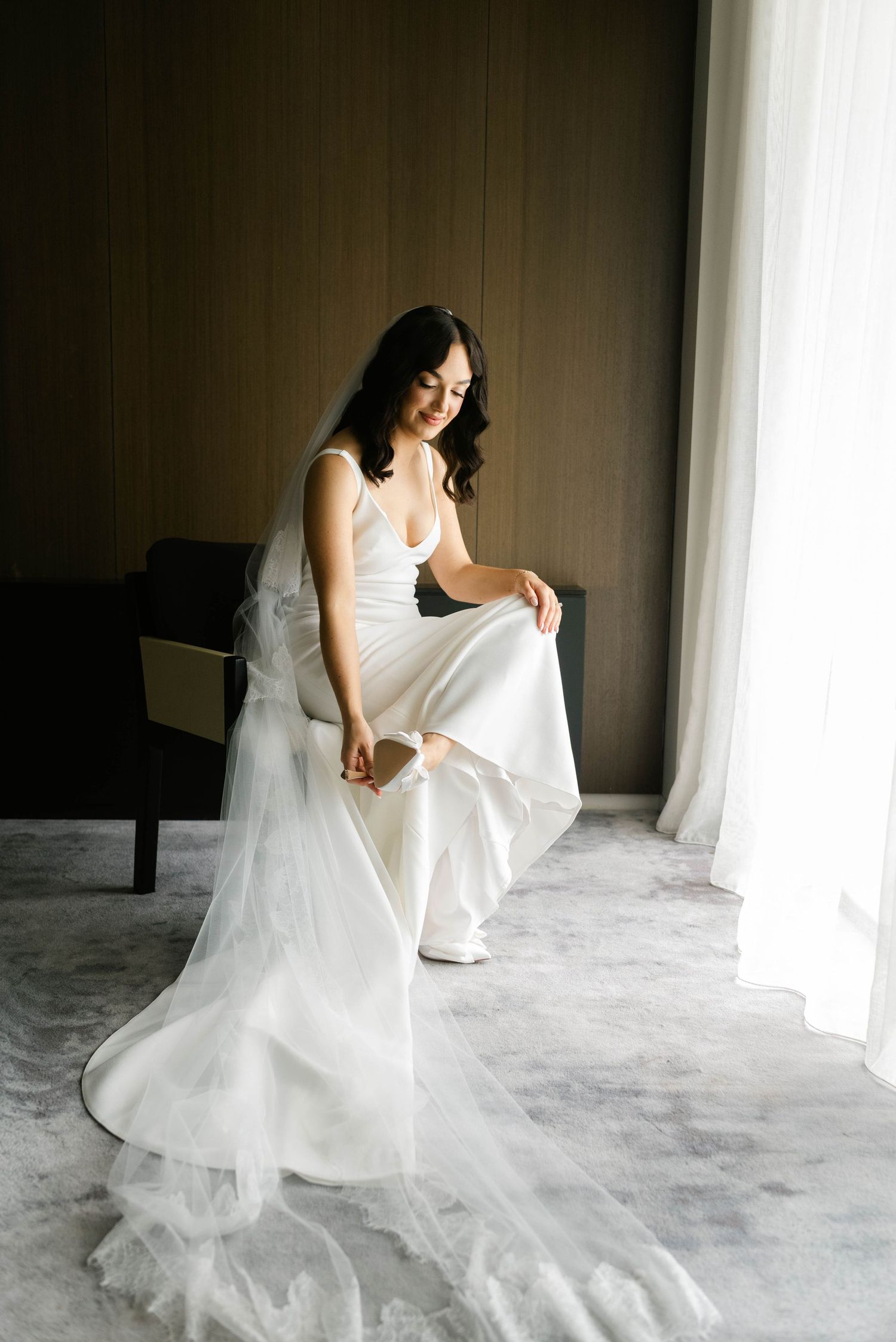 A flowing white wedding dress with layers of tulle fabric creates an ethereal silhouette against a neutral backdrop.